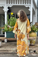 Back view of our 70s inspired maxi kaftan-style dress with bell sleeves , retro patch pockets and a v-neckline. Features a bold, large-scale  retro geo print. in rich mustard and brown tones. Made in 100% cotton