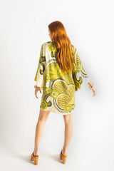 Back view of our 60s inspired mini smock dress with bell sleeves, patch pockets and a v-neckline. Features a bold, large-scale retro geo print. in rich green tones. Made in 100% cotton