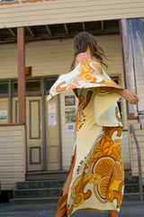 Bohemian style one shoulder maxi dress featuring a long, flowy frill that covers one arm and drapes elegantly down to the hips. This dress has side splits and showcases a large-scale bold, retro inspired print in rich mustard, brown and cream tones. Made in 100% rayon.