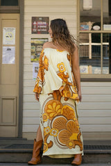 Bohemian style one shoulder maxi dress featuring a long, flowy frill that covers one arm and drapes elegantly down to the hips. This dress has side splits and showcases a large-scale bold, retro inspired print in rich mustard, brown and cream tones. Made in 100% rayon.