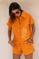 With and oversized 70s retro collar this button up terry towelling shirt with coconu buttons gives full 70s vibes. Worn with the matching shorts it's the perfect retro shirt and shorts set. Tangerine with hand screen palm print. Cotton / elastane blend