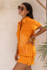 With an oversized 70s retro collar this button up terry towelling shirt with coconut buttons gives full 70s vibes. Worn with the matching shorts it's the perfect retro shirt and shorts set. Tangerine with hand screen palm print. Cotton / elastane blend