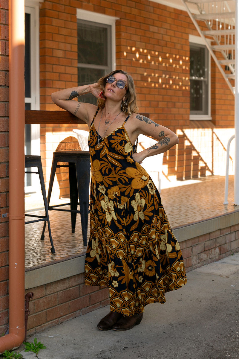 V-neck bohemian style floaty maxi dress with a low v-back and double layered frills in a large scale floral print in brown and gold tones with a black background