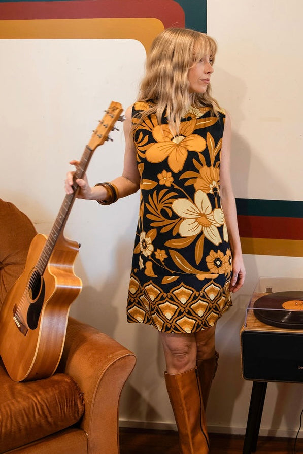 Bold floral vintage style mini dress in a soft rayon voile with high bateau neckline and retro  large scale brown and gold tone flowers on a black background