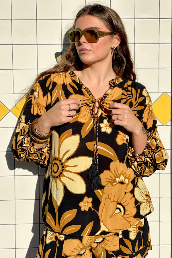 Vintage inspired bohemian blouse with a v- neckline and tie details in a large scale floral print in brown and gold tones with a black background