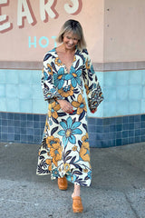 70s vintage inspired boho midi dress with bold retro floral print in blue,tan and navy on a cream background, bell sleeves and side splits. Made in rayon