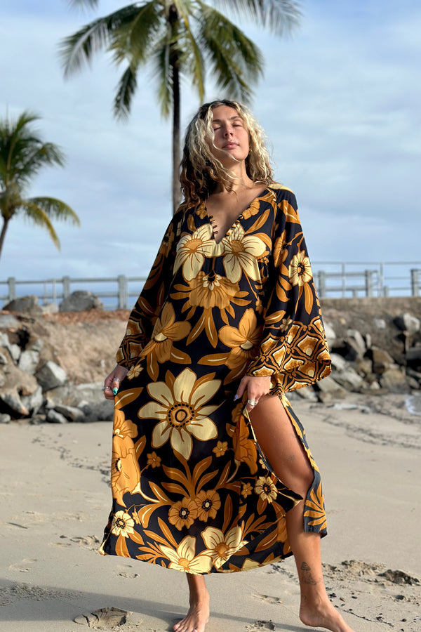70s vintage inspired boho midi dress with bold retro floral print in brown,gold and cream tones on a black background, bell sleeves and side splits. Made in rayon
