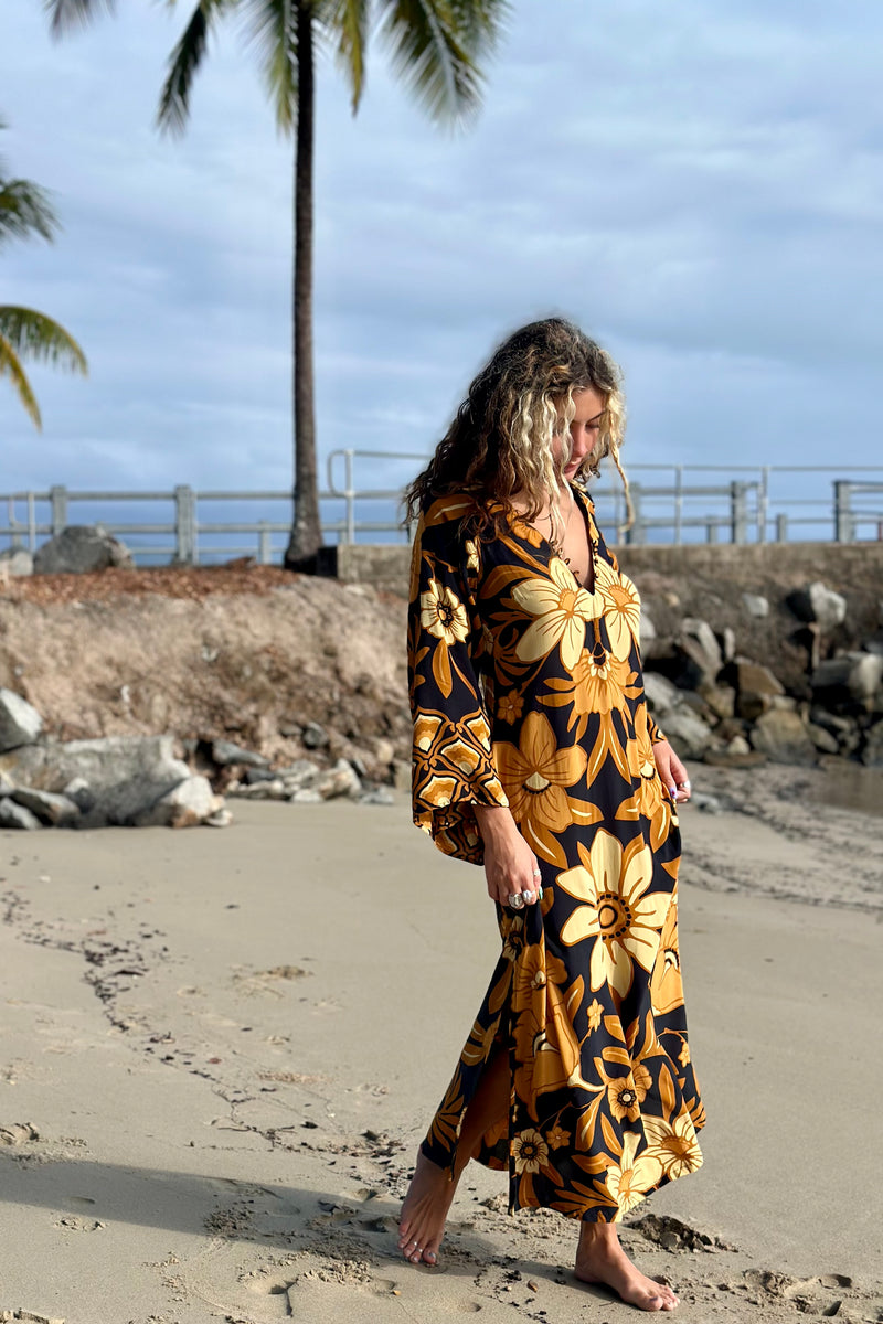 70s vintage inspired boho midi dress with bold retro floral print in brown,gold and cream tones on a black background, bell sleeves and side splits. Made in rayon