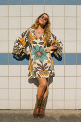 70s vintage inspired boho mini dress with bold retro floral print in blues and mustard on a cream background, bell sleeves and side splits. Made in rayon