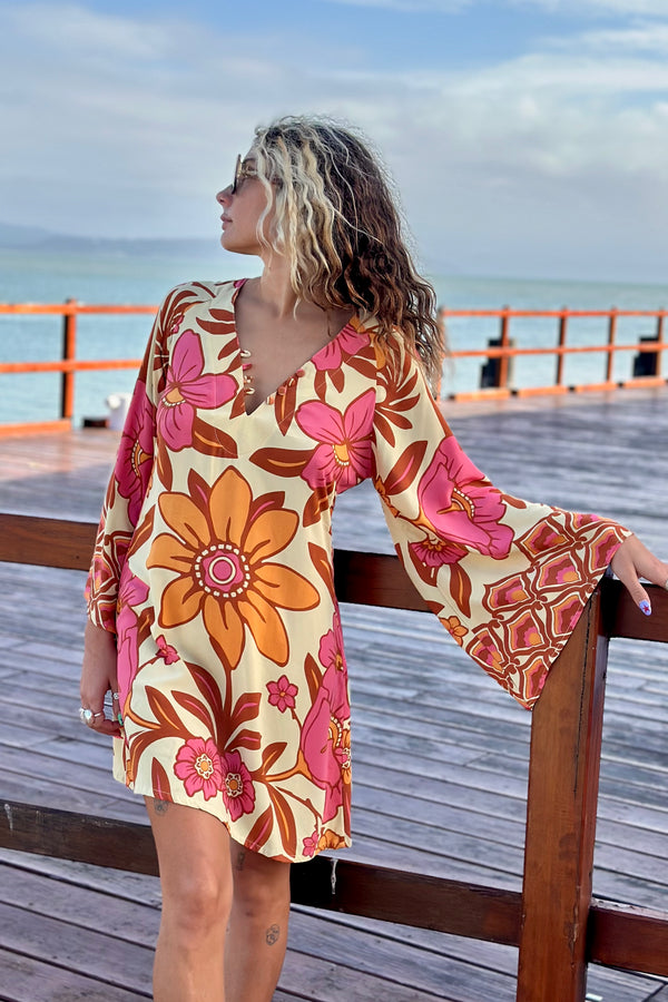 70s vintage inspired boho mini dress with bold retro floral print in Pink and orange tones on a buttery cream background, bell sleeves and side splits. Made in rayon