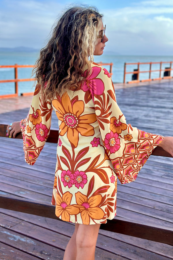 70s vintage inspired boho mini dress with bold retro floral print in Pink and orange tones on a buttery cream background, bell sleeves and side splits. Made in rayon