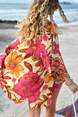 Vintage inspired bohemian style button up smock dress  worn unbuttoned as a kaftan in a large scale floral print in pink and orange with a buttery cream  background