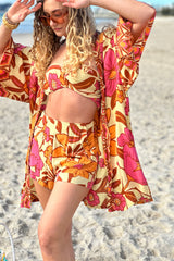 Vintage inspired bohemian style button up smock dress  worn unbuttoned as a kaftan in a large scale floral print in pink and orange with a buttery cream  background