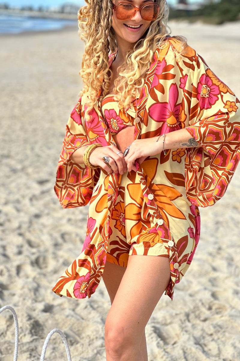 Vintage inspired bohemian style button up smock dress  worn unbuttoned as a kaftan in a large scale floral print in pink and orange with a buttery cream  background