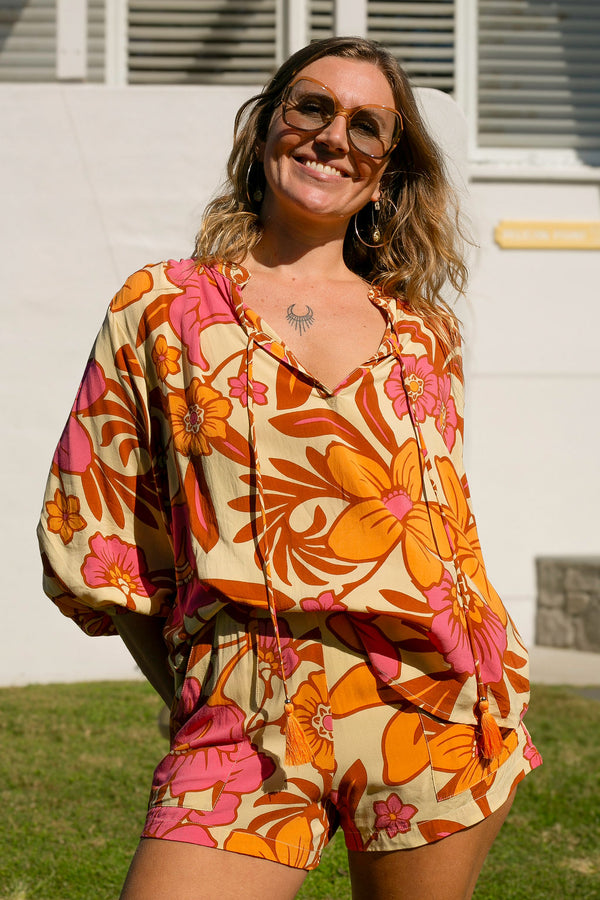 Vintage inspired bohemian style blouse with a v neckline and detail ties in a large scale retro floral print pink and orange flowers on a buttery cream background