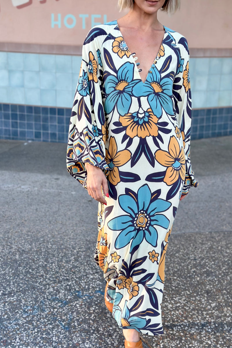 70s vintage inspired boho midi dress with bold retro floral print in blue,tan and navy on a cream background, bell sleeves and side splits. Made in rayon