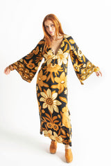70s vintage inspired boho midi dress with bold retro floral print in brown,gold and cream tones on a black background, bell sleeves and side splits. Made in rayon