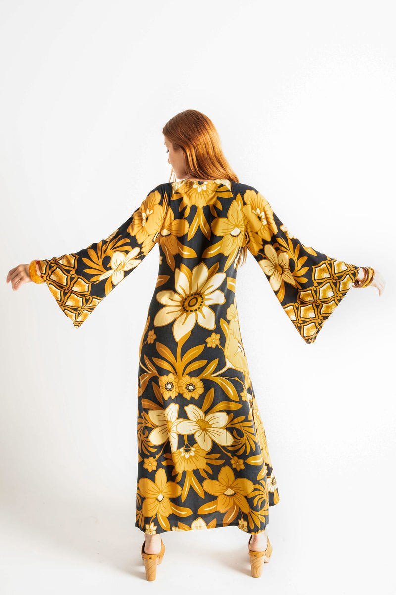 70s vintage inspired boho midi dress with bold retro floral print in brown,gold and cream tones on a black background, bell sleeves and side splits. Made in rayon